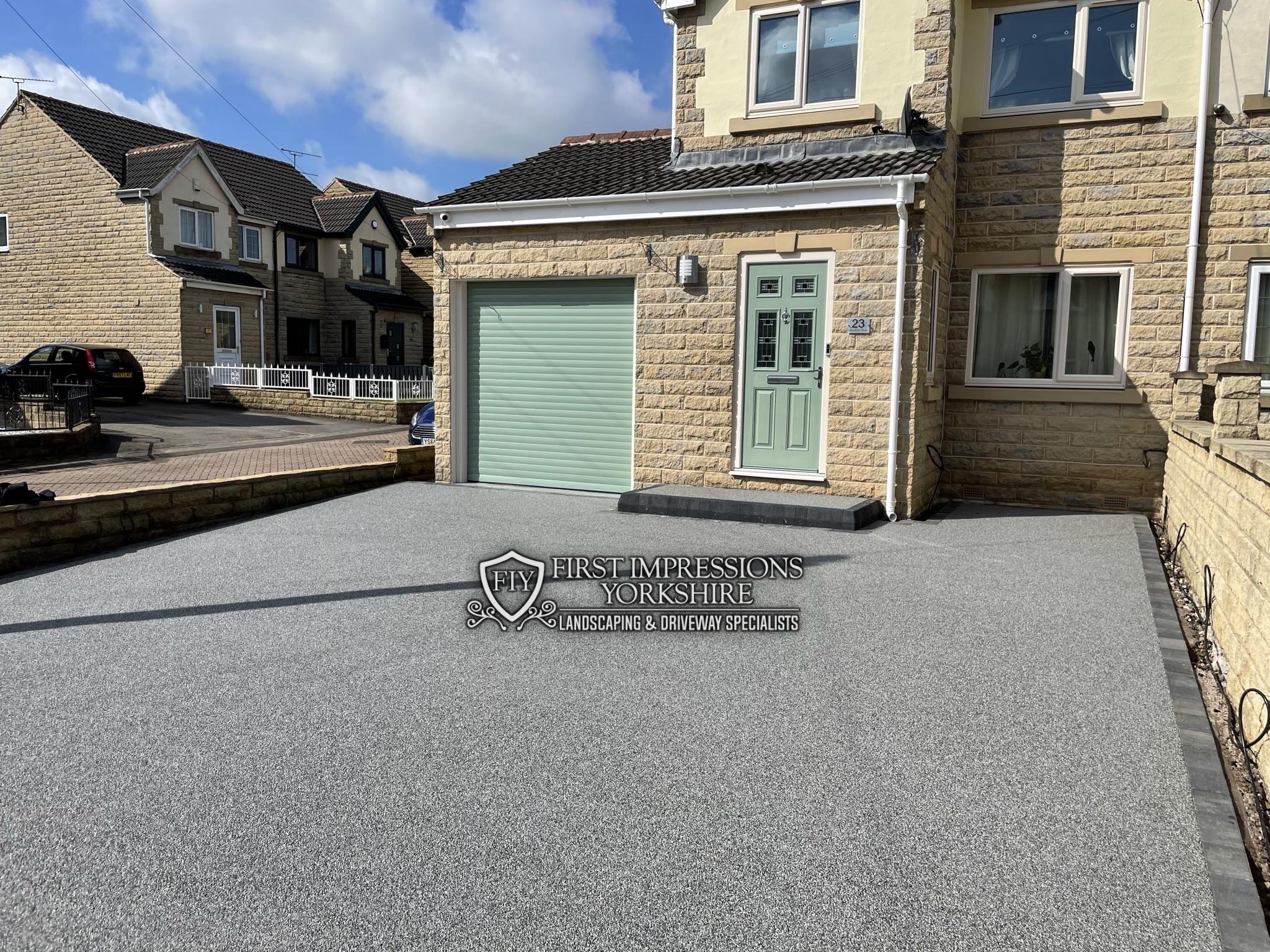 Silver grey resin bound driveway to a stone fronted house with a green garage door
